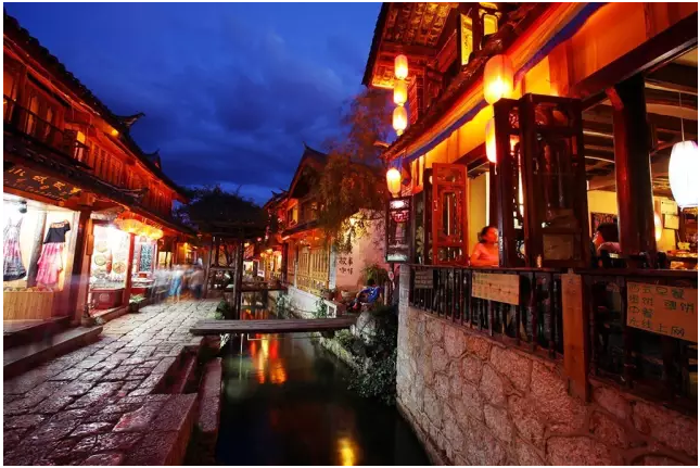 图:大研古镇街道夜景 现在大研的很多古建也都被改造成酒吧和客栈,现代娱乐方式的侵入,给大研原本的淳朴与宁静增添了新的风情,也改变了古城的文化氛围。 没有城墙的大研古城,三山为屏、一川相连 大研古城依山而建,街巷依水流而设,街道用红色角砾岩(五花石)铺就,下雨地不会泥、晴天也不会有浮尘,石上花纹图案自然雅致,质感细腻,与整个环境相得益彰。 很独特的一点,大研古城是一座没有城墙的古城,据说是因为丽江世袭统治者姓木,筑起城墙就象木字加框而成困,十分不吉利,城内也没有中规中矩的道路网;同时古城的布局体现了典型